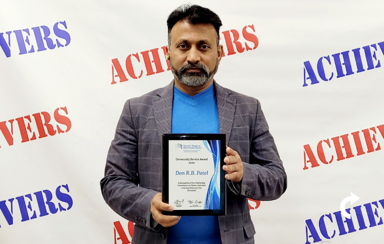 Don Patel standing in front of an Achievers backdrop holding his 2022 Community Service Award