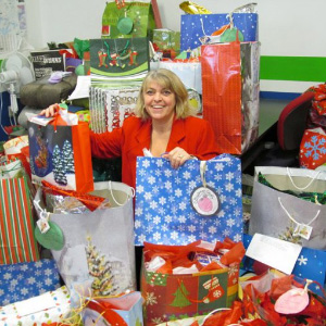 Woman in a red jacket in the middle of Christmas presents.