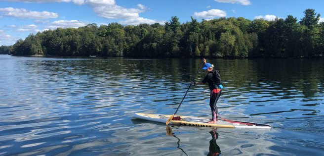 Jennifer Evelyn paddle boarding on a lake.