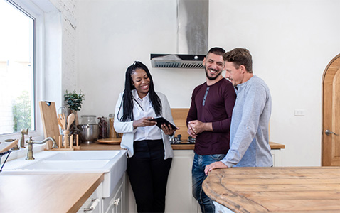 African American female real estate agent in kitchen showing a gay couple around a new house